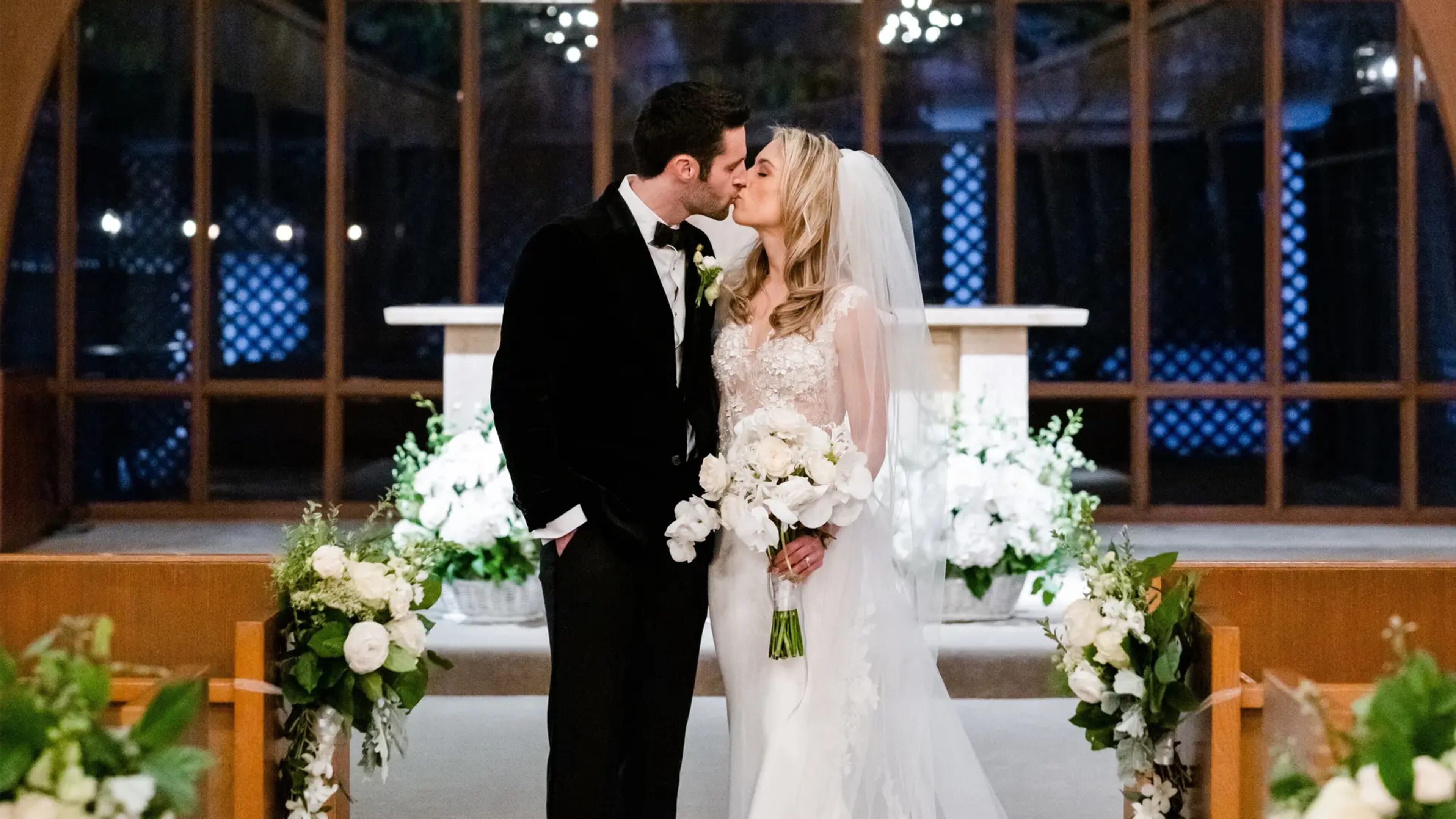 Bride and groom kissing at an altar decorated with white flowers by Frangipani Florist